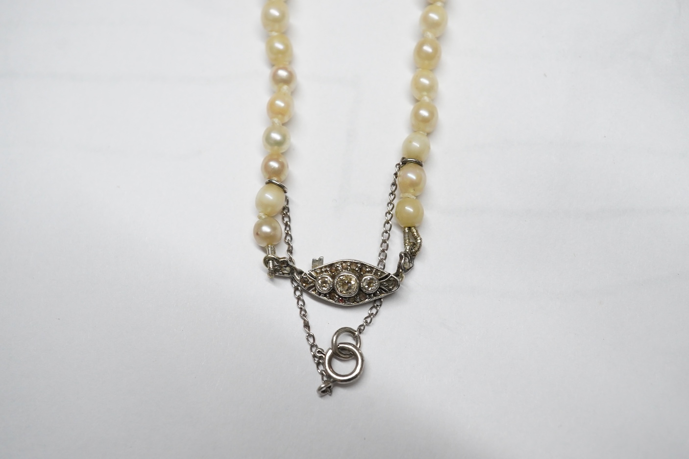 A single strand graduated cultured pearl choker necklace, with a three stone diamond set engraved white metal clasp, 36cm